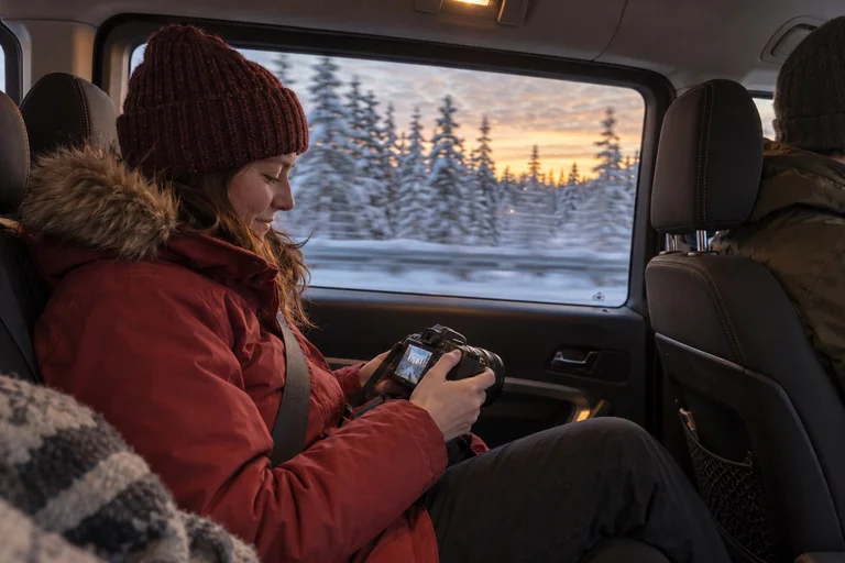 Generated illustration of a passenger reviewing camera photographs as snowy forest passes outside the minivan