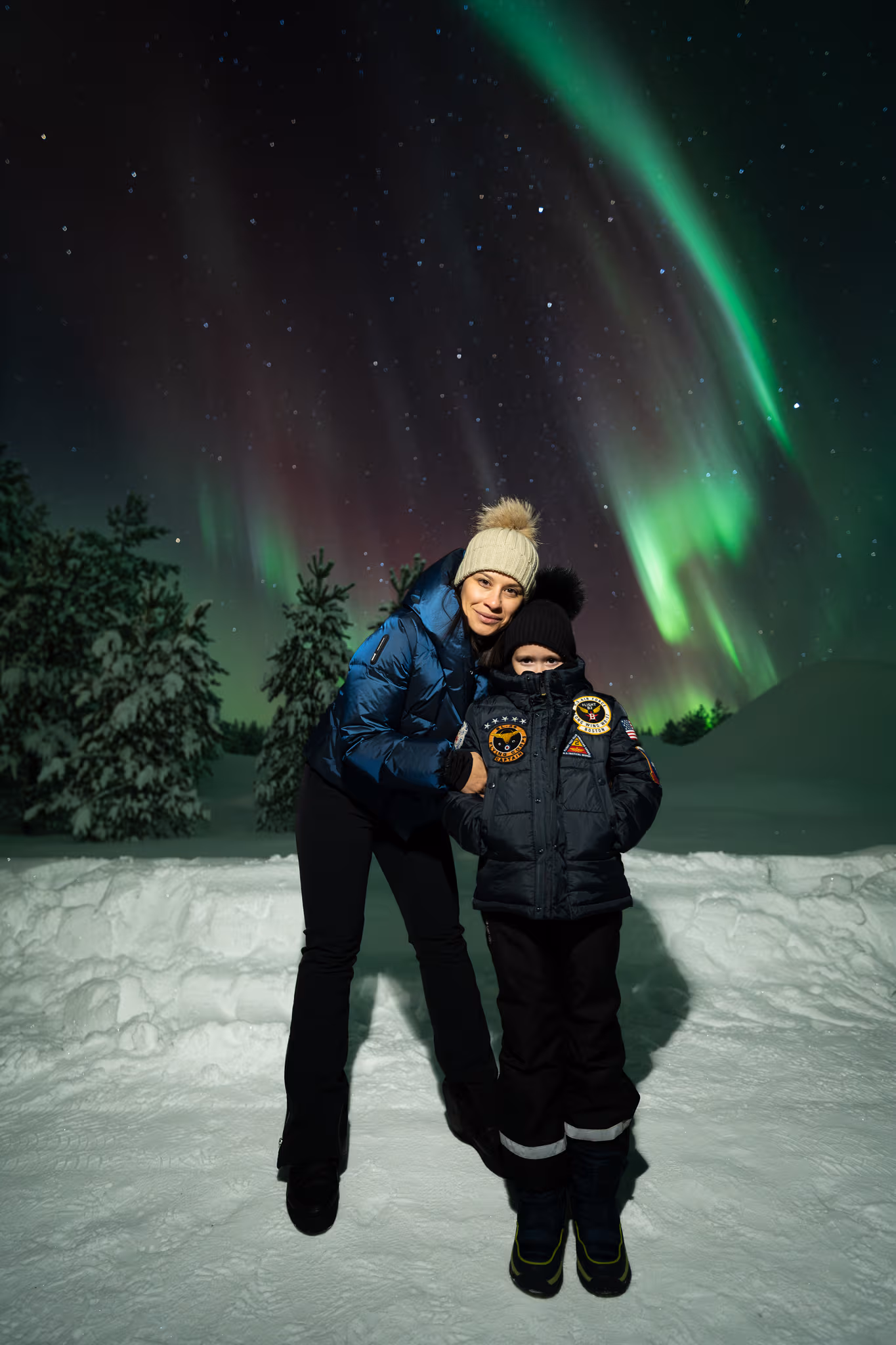 Two guests jumping in the snow beneath green aurora