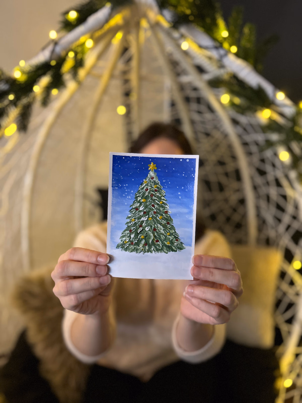Guest holding a hand-painted Christmas tree postcard